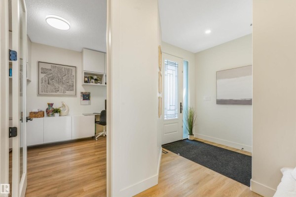 View from hallway into a home office with built-in cabinets and desk, and the front entrance with glass door. - 108 Edgefield Wy, St  Albert