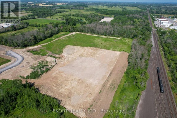 Aerial view of cleared land with railway nearby, showcasing surrounding green fields and trees. - 108 Huff Avenue, Quinte West