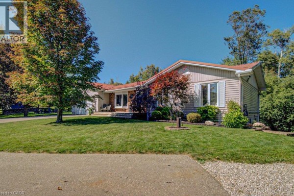 Side view of the house showing a manicured lawn, trees, and a covered porch area. - 108 Lake Road, Puslinch