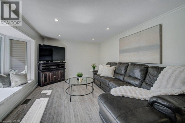 Living room featuring a large black leather sectional sofa, glass coffee table, and bay window. - 108 Lake Road, Puslinch