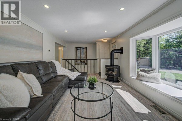 Living room with dark leather sofa, black wood-burning stove, and large bay window with seating. - 108 Lake Road, Puslinch