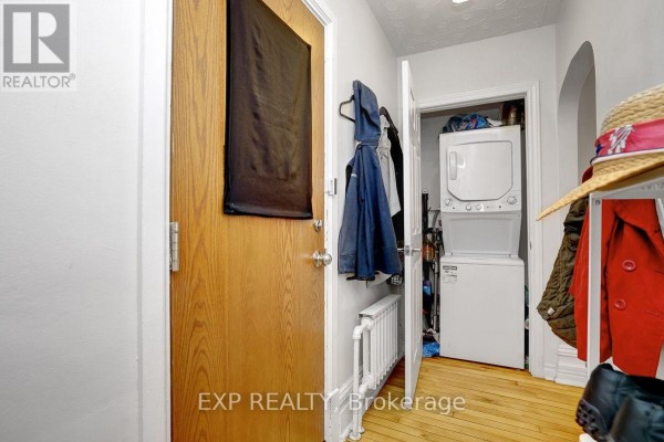 Hallway showing a wooden door, stacked washer and dryer, and shelving. - 108 Lebreton Street N, Ottawa