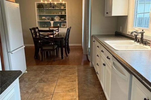 Kitchen with white cabinets, black countertops, double sink, dishwasher, and large window overlooking backyard. - 108 Stothart Drive, Miramichi