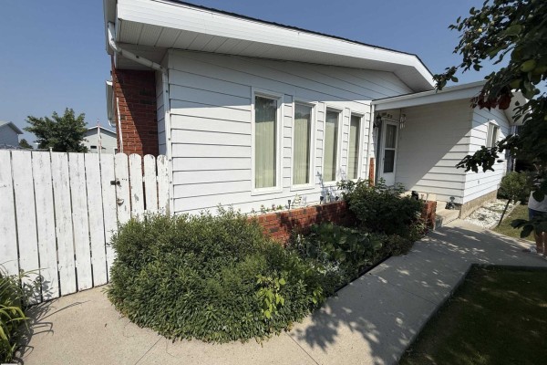 Side view of the bungalow showing white siding and a white picket fence. - 10808 109 Street, Westlock