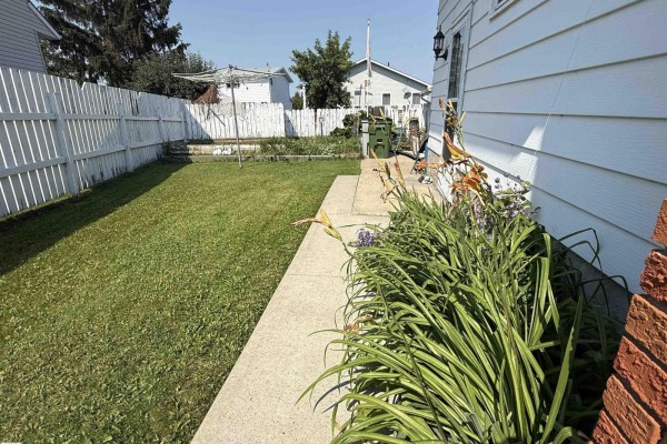 Backyard view with green grass, concrete path, and white fence. - 10808 109 Street, Westlock