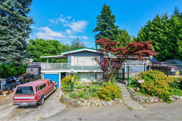 Aerial view of a suburban neighborhood with a main road and distant city skyline including a suspension bridge. - 10810 129 Street, Surrey