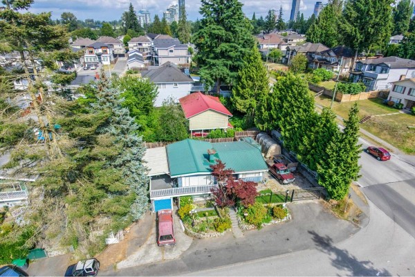 Top-down aerial view of a house with a green metal roof, surrounded by trees and storage sheds. - 10810 129 Street, Surrey
