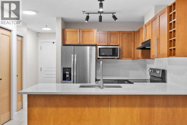 Modern kitchen with stainless steel refrigerator, wood cabinets, and quartz countertops. - 1083 Sunset Drive Unit# 211, Kelowna