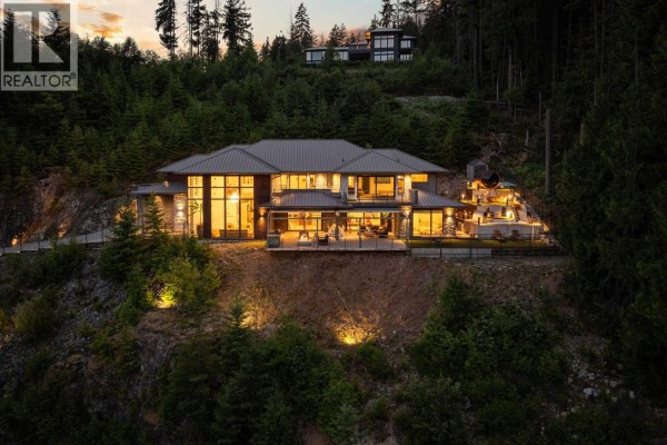 Expansive view of the luxury residence nestled into a forested hillside at sunset. - 1083 Uplands Drive, Anmore