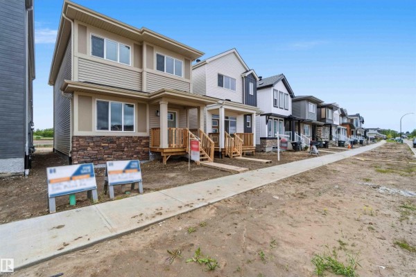 Street view of a row of unfinished townhouses on a dirt road with a sidewalk. - 1084 Mcleod Av, Spruce Grove