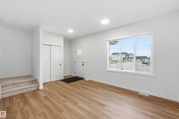 Open-concept living space with light wood floors, white walls, stairs, and kitchen area. - 1084 Mcleod Av, Spruce Grove