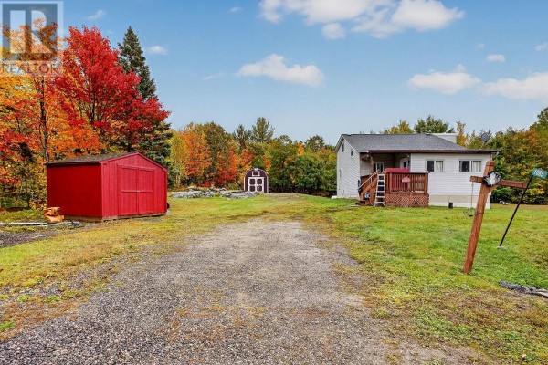 Gravel driveway leading to a white house with a wooden deck and red storage sheds. - 1085 St. Cloud Road, Wahnapitae