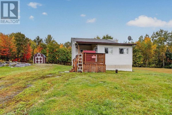 Side view of a white house with a wooden deck, surrounded by a grassy lawn and trees. - 1085 St. Cloud Road, Wahnapitae