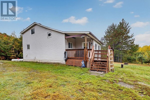 Rear view of a white house with a deck and propane tank, set in a wooded landscape. - 1085 St. Cloud Road, Wahnapitae