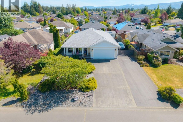 Small, white garden shed with a dark door and windows, surrounded by trees. - 1085 Tara Cres, Parksville
