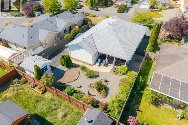 Front entrance of a house with a dark door, covered porch with stone pillars, and landscaping. - 1085 Tara Cres, Parksville