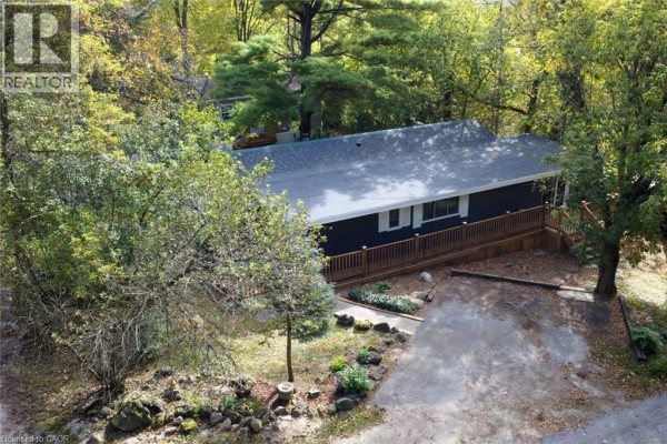 Aerial view of the dark-sided mobile home with a wooden deck nestled among trees. - 1085 W Concession 10 Concession W Unit# 99, Flamborough