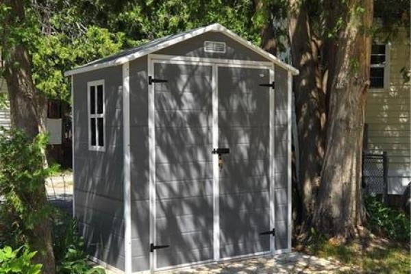 A grey storage shed with double doors and a small window sits beside large trees. - 1085 W Concession 10 Road Unit# 29, Flamborough