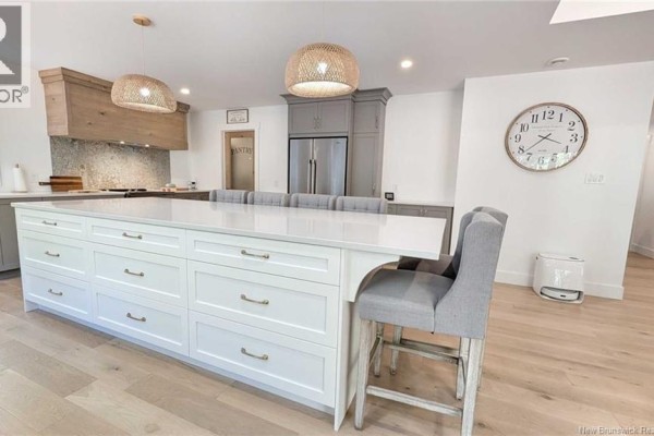 A large white kitchen island with seating faces grey cabinetry and stainless steel appliances. - 10858 Nb-11, Pokemouche