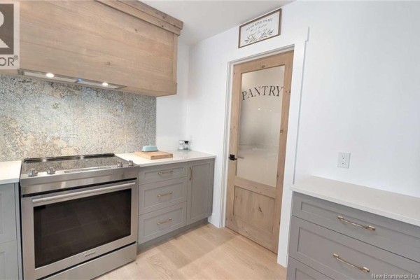 A stainless steel stove is next to grey cabinets and a frosted glass pantry door. - 10858 Nb-11, Pokemouche