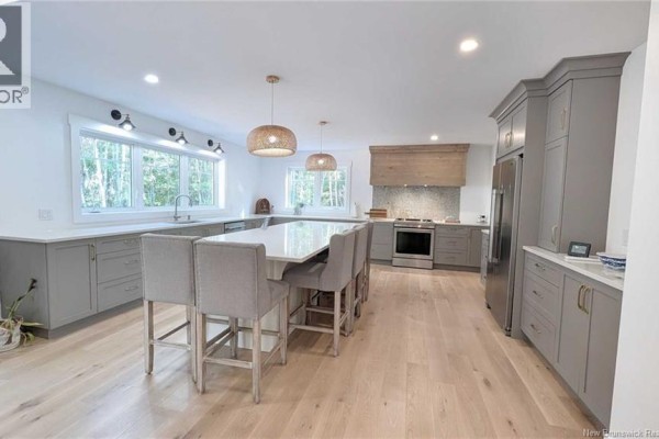 A spacious, modern kitchen features a large island, grey cabinets, and a stainless steel range. - 10858 Nb-11, Pokemouche