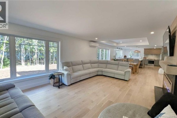 A light grey sectional sofa faces a fireplace and large windows overlooking a wooded area. - 10858 Nb-11, Pokemouche