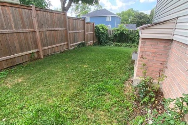 Narrow backyard with green grass, wooden fence, and a portion of the house exterior. - 1087 Brookview Crescent, Windsor