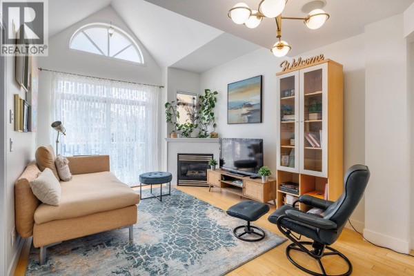Living room with a beige sofa, fireplace, and large windows allowing natural light. - 1088 Sunset Drive Unit# 247, Kelowna