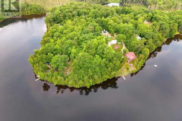 Aerial view of a tree-covered island property with several buildings and docks on the water. - 1089 Prince Lake Rd, Prince Township