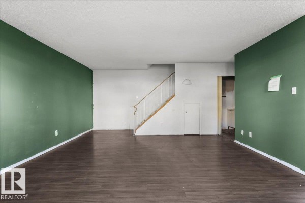 Empty living room with dark wood laminate flooring and green accent wall. - #108a 14520 52 St Nw, Edmonton
