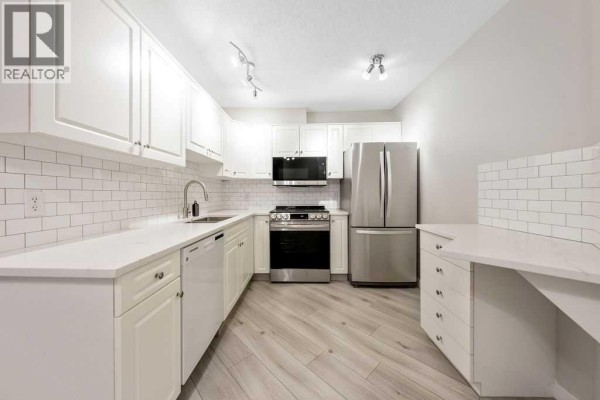 White kitchen with subway tile backsplash, stainless steel appliances, and light wood laminate flooring. - 109, 20 Sierra Morena Mews Sw, Calgary