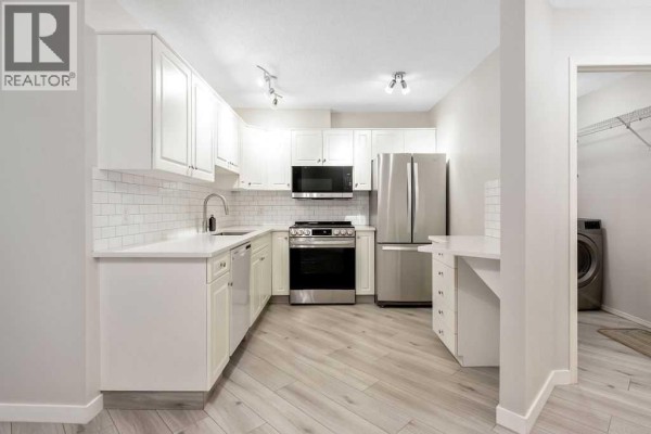 View of the white kitchen and entryway with a washer and dryer visible. - 109, 20 Sierra Morena Mews Sw, Calgary