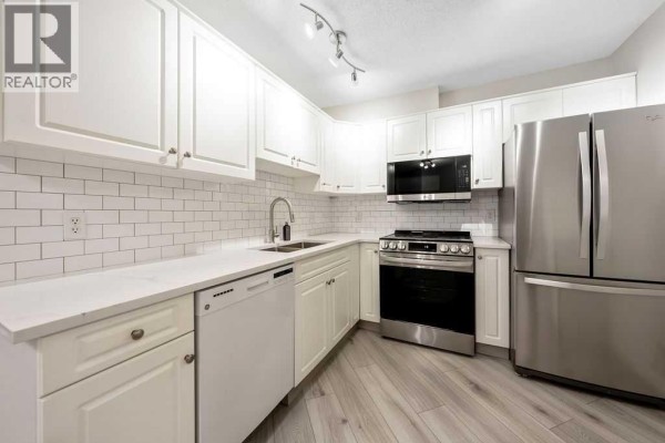 White kitchen with white cabinets, white quartz countertops, and stainless steel appliances. - 109, 20 Sierra Morena Mews Sw, Calgary