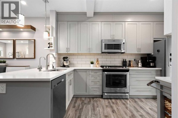 Spacious kitchen with stainless steel refrigerator, light grey cabinetry, and a view into the living area. - 109, 355 Nolancrest Heights Nw, Calgary