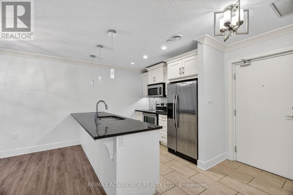 View of kitchen island with sink, cabinetry, stainless steel refrigerator, and entryway. - 109 - 320 Sugarcreek Trail, London North