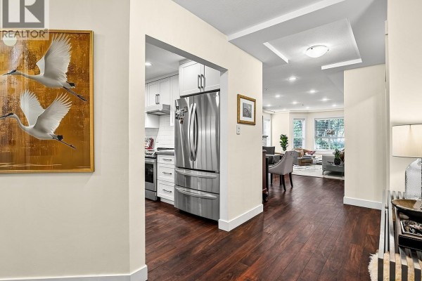 View from hallway to kitchen with stainless steel appliances and living area beyond. - 109 1283 Parkgate Avenue, North Vancouver