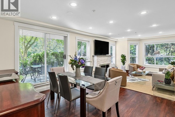 Dining area with glass table, grey chairs, and living area with fireplace and patio access. - 109 1283 Parkgate Avenue, North Vancouver