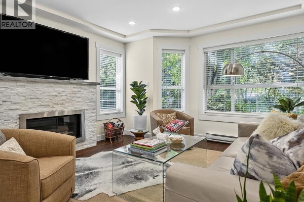 Living room with sofa, chairs, glass coffee table, and stone-clad fireplace with television. - 109 1283 Parkgate Avenue, North Vancouver