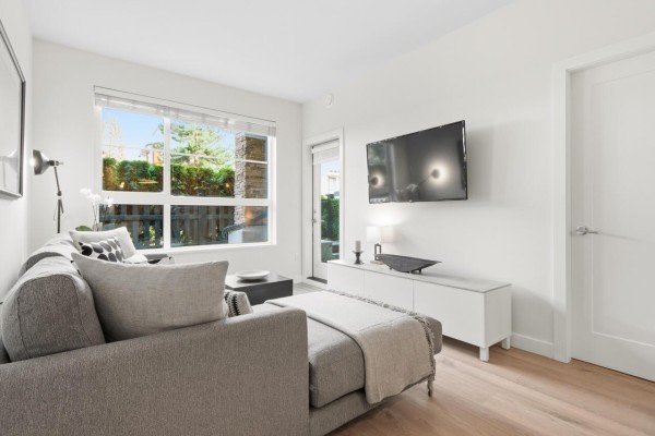 Bright living space featuring a gray sofa, TV, and access to outdoor area - 109 20829 77a Avenue, Langley