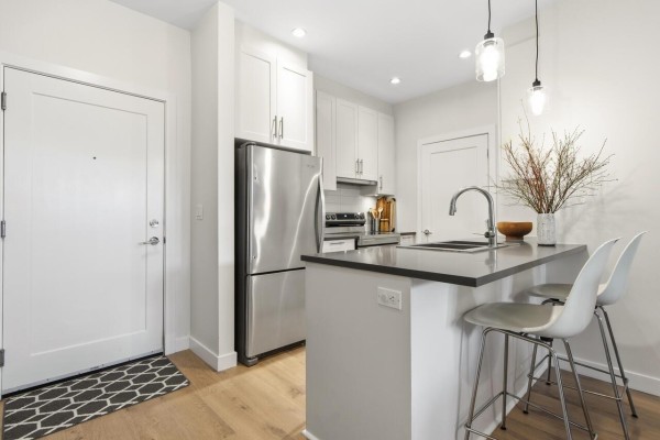 Modern kitchen with stainless steel appliances, white cabinetry, and breakfast bar - 109 20829 77a Avenue, Langley
