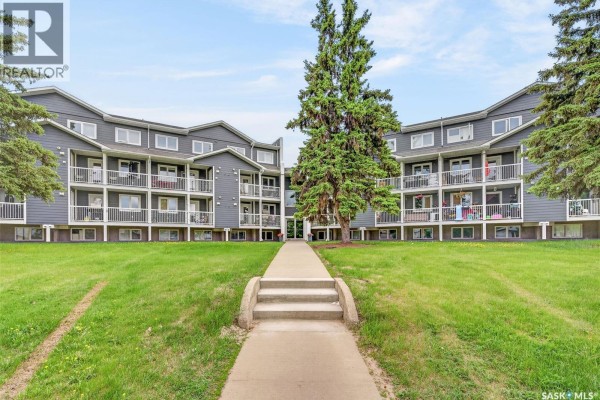 Pathway leading to the entrance of a grey apartment building with green lawn. - 109 515 28th Street E, Prince Albert
