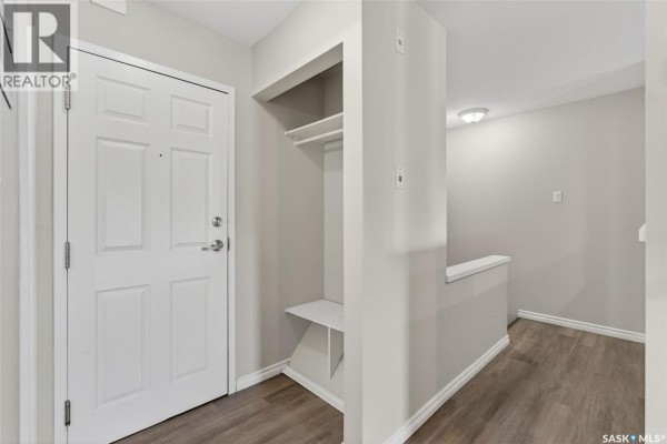 Apartment entryway with a white door, built-in shelf, and wood-look flooring. - 109 515 28th Street E, Prince Albert