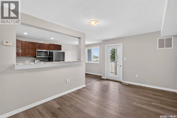 Open-concept living area and kitchen with dark wood cabinets and white countertops. - 109 515 28th Street E, Prince Albert