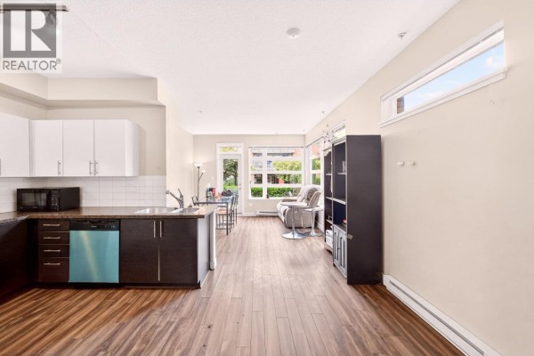 Open-concept living area with kitchen, dining area, and sofa facing large windows. - 109 5692 Kings Road, Vancouver