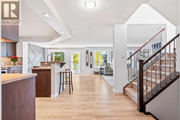 Open concept main floor with light wood flooring, a kitchen island, and a staircase. - 109 Drake Landing Cove, Okotoks