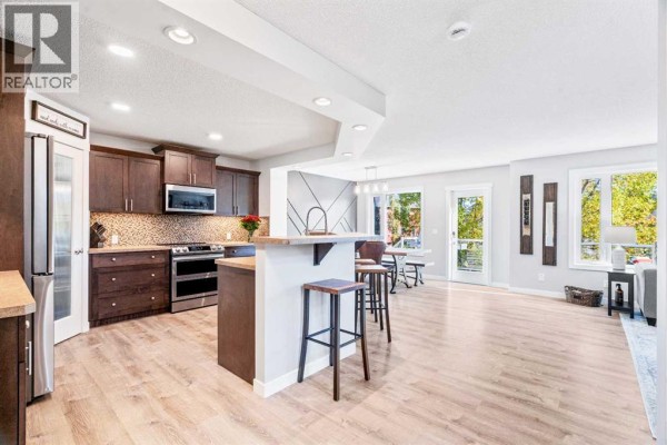 Kitchen with dark wood cabinets, stainless steel appliances, a tiled backsplash, and an island. - 109 Drake Landing Cove, Okotoks