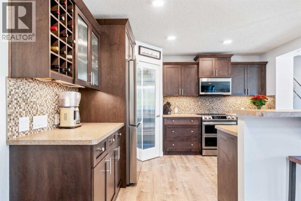 Dark wood kitchen cabinets, stainless steel appliances, a tiled backsplash, and a wine rack feature. - 109 Drake Landing Cove, Okotoks
