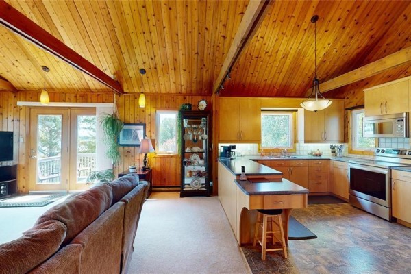Living room and kitchen with wood-paneled walls, vaulted ceiling, and island. - 109 Elm Avenue E, Winnipeg Beach
