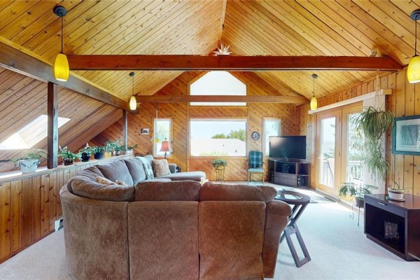 Living room with a large sectional sofa, television, and doors leading to a deck. - 109 Elm Avenue E, Winnipeg Beach
