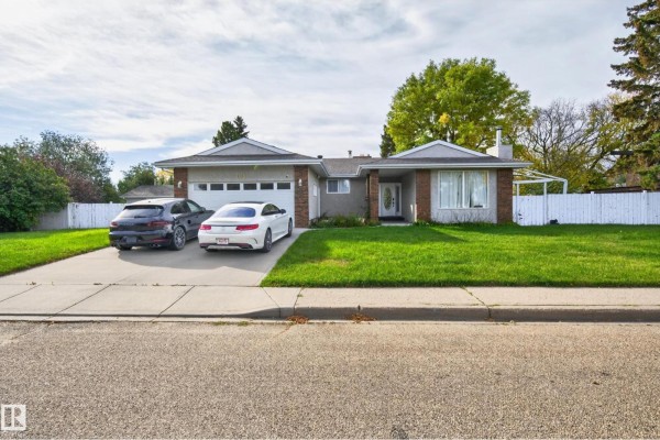 Front exterior of a bungalow with a large lawn, paved driveway, and two cars parked. - 109 Evergreen Cr, Wetaskiwin